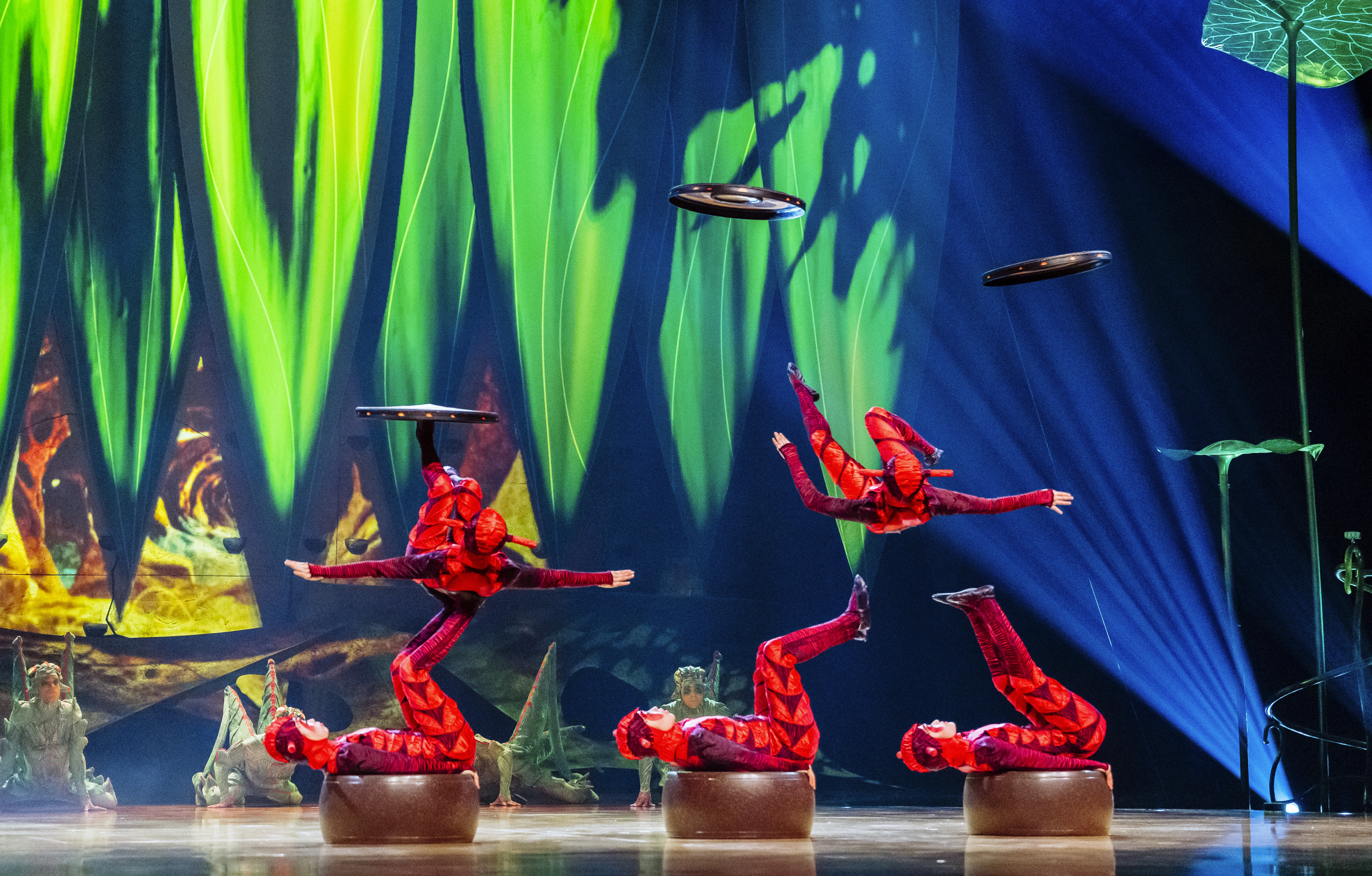 Performers at Cirque du Soleil OVO juggle other performers on their outstretched legs as those performers juggle plates with their legs